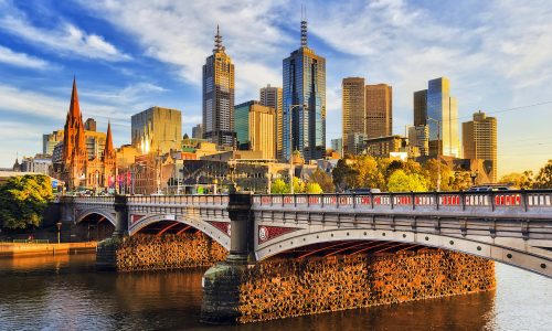 Warm morning light on high-rise towers in Melbourne CBD above Princes bridge across Yarra river.